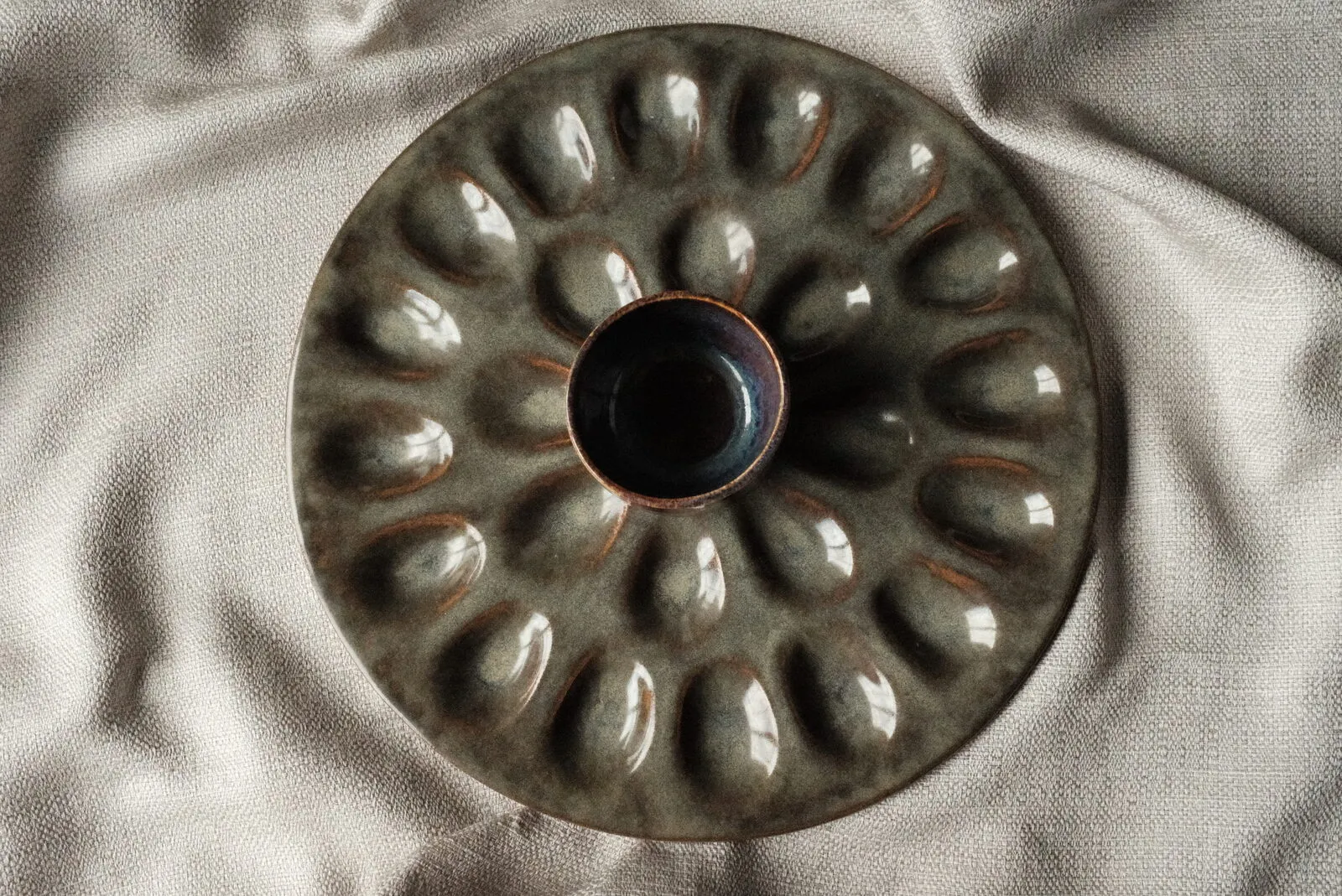 A hand-glazed stoneware deviled-egg plate resting on soft linen