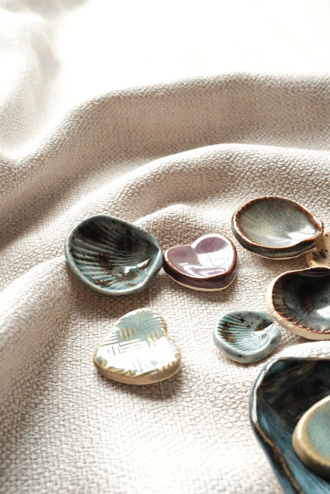 An overhead spread of Kelly's hand-built shell and heart dishes in soft coastal glazes, resting on woven linen