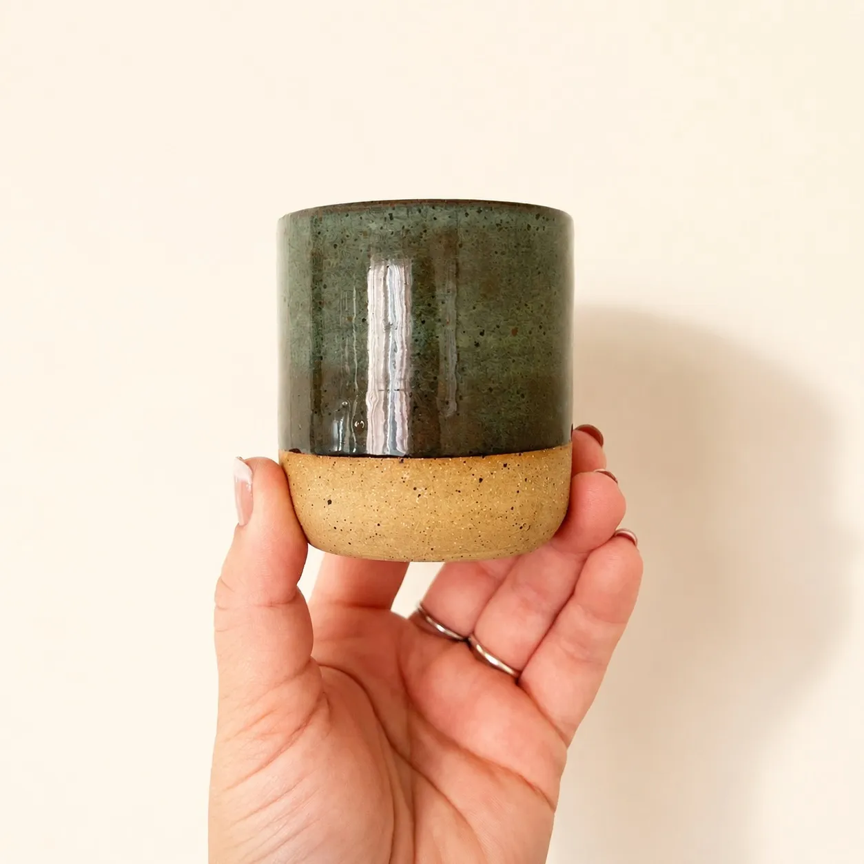 A hand-glazed green stoneware tumbler held in hand