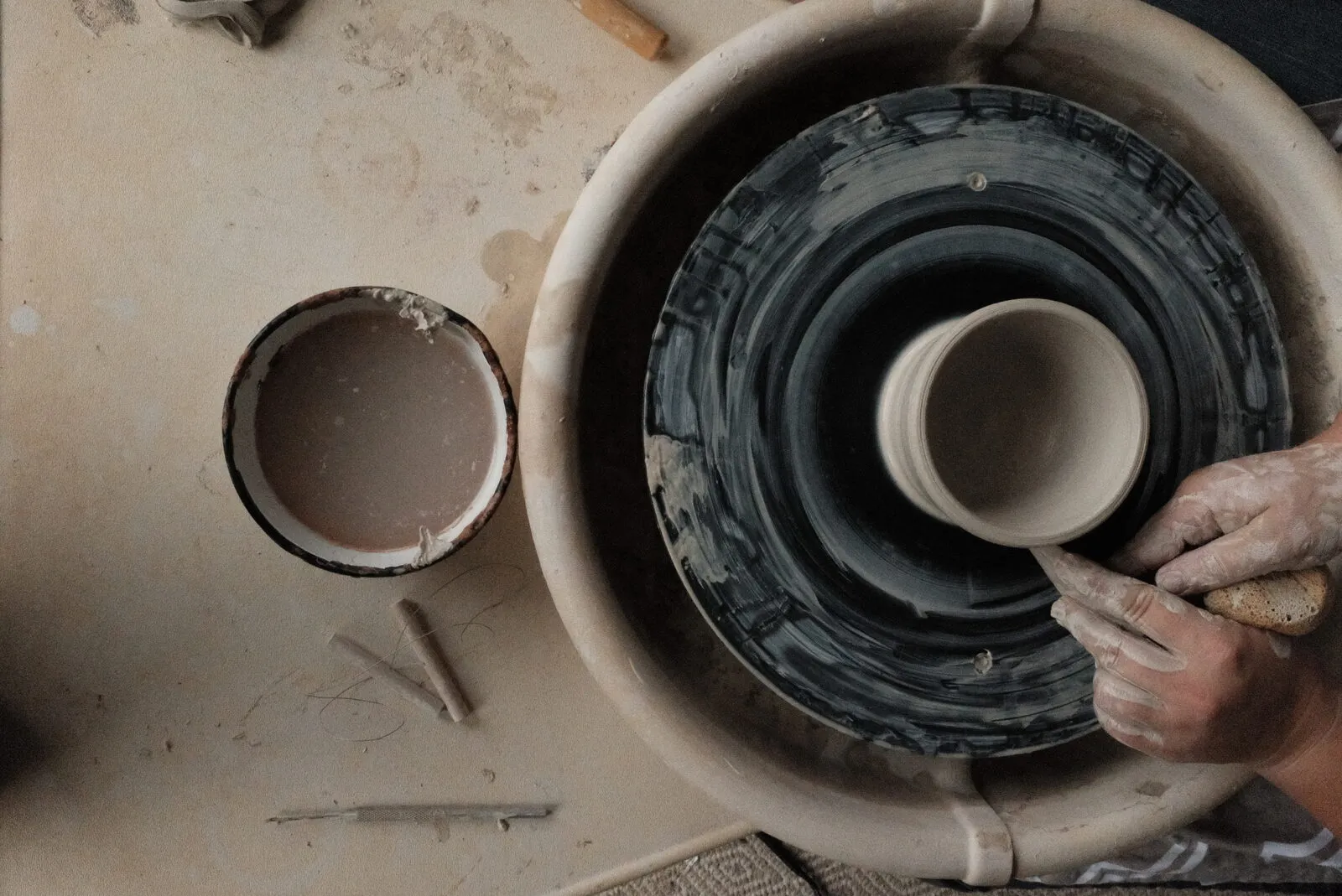 Overhead view of clay-covered hands shaping a vessel on the wheel at a Devine Perks one-on-one class