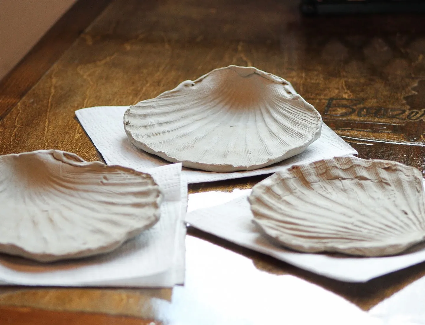 Hand-pressed clay seashell dishes drying on a table before glazing