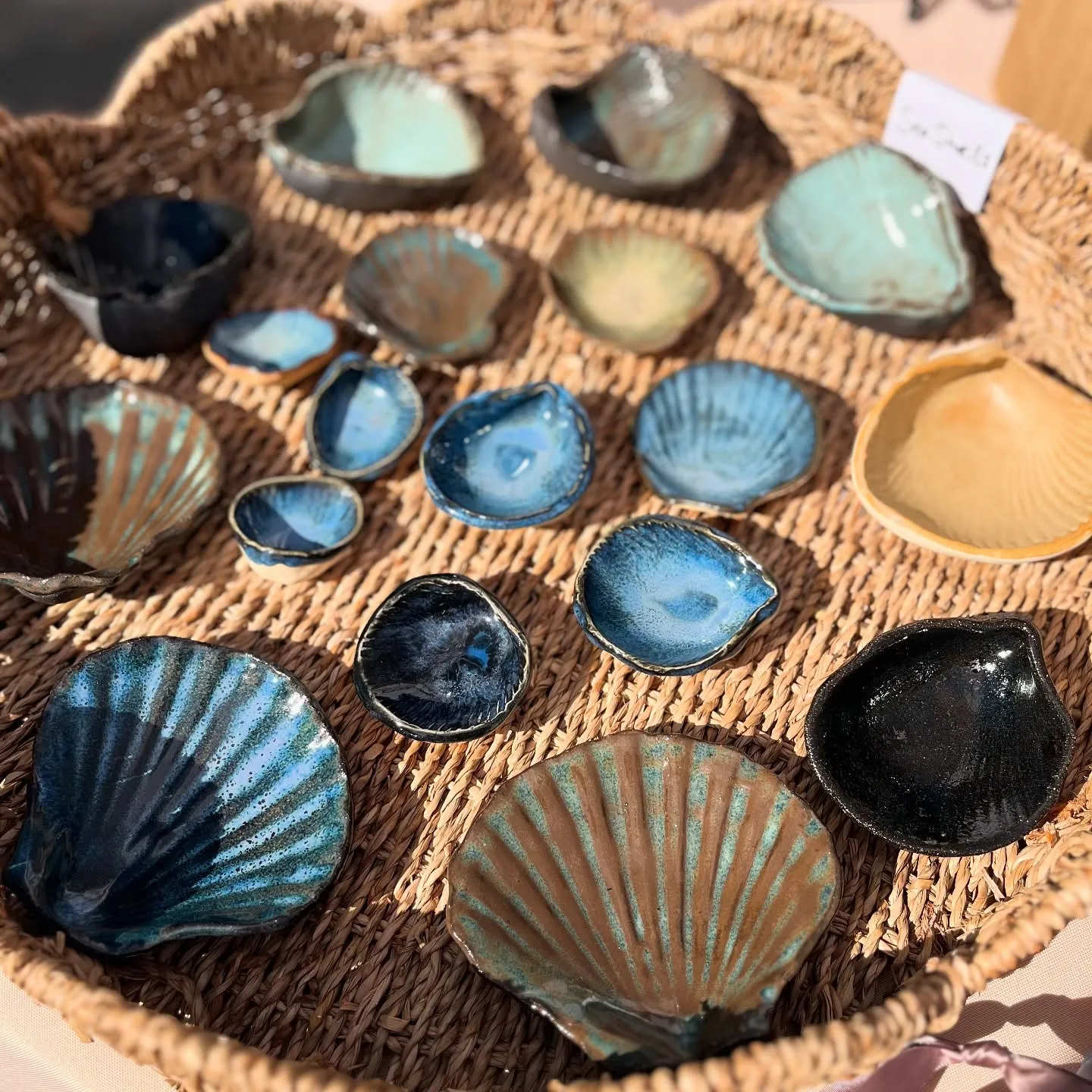 An assortment of Kelly's blue-glazed ceramic seashell dishes arranged in a woven basket