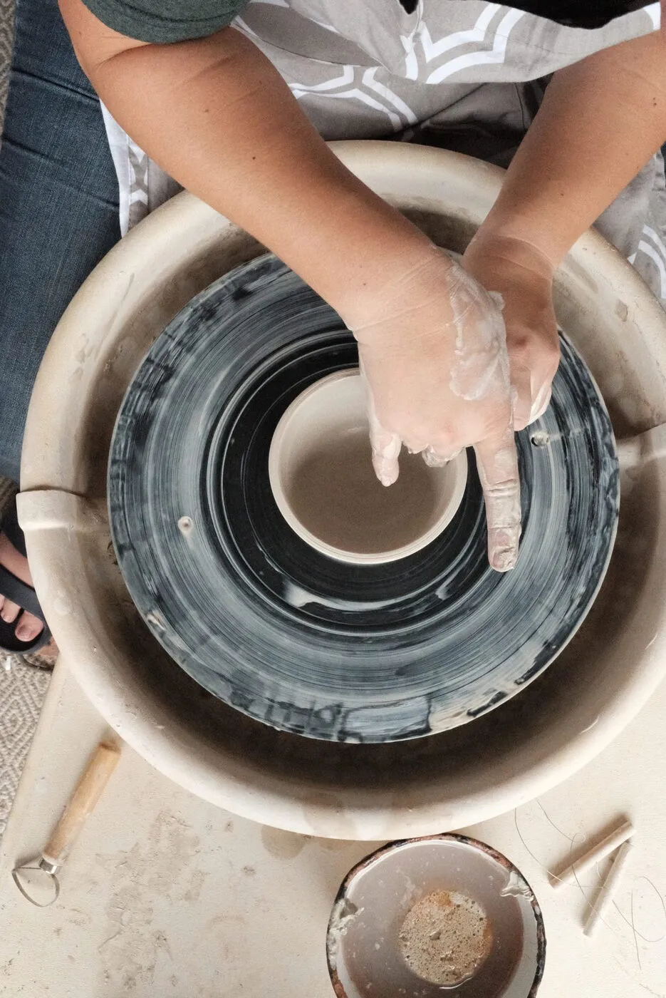 Kelly's clay-covered hands shaping a pot on the wheel, seen from above