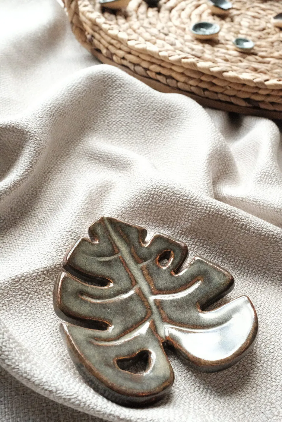 A hand-glazed sage monstera-leaf dish resting on soft linen