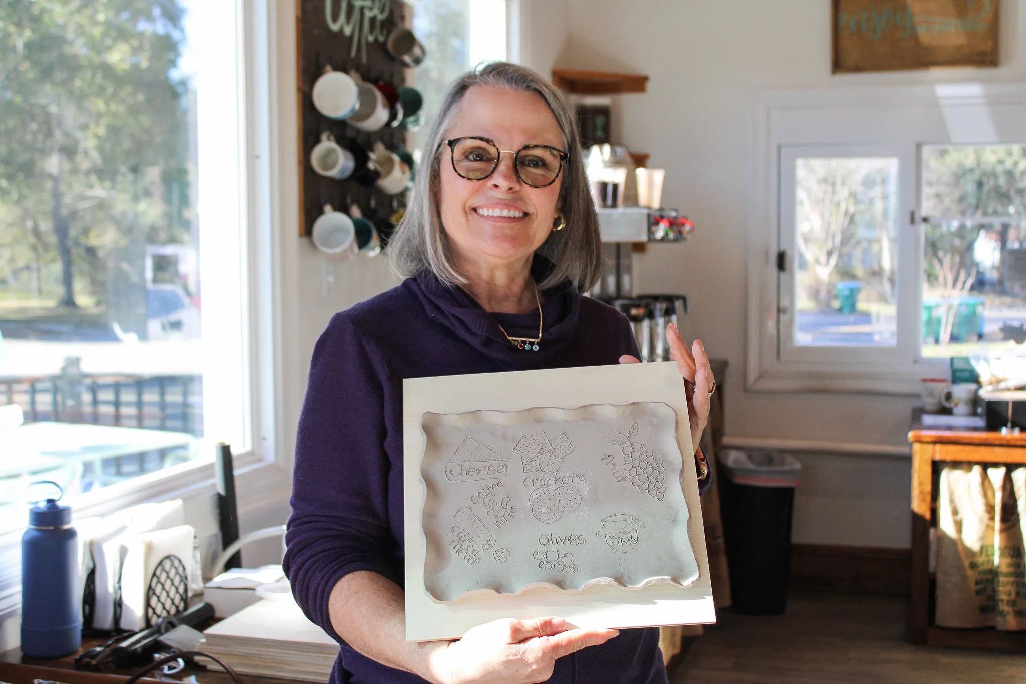 A student holding the carved charcuterie board she made at a Devine Perks workshop