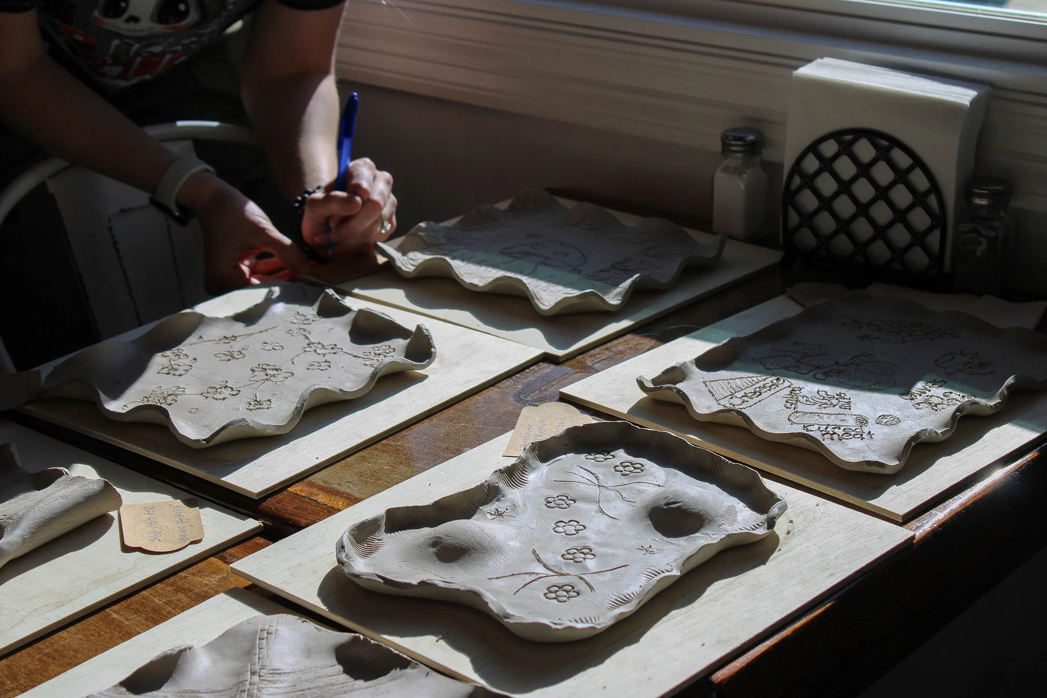 Hands carving botanical designs into clay trays at a Devine Perks pottery workshop