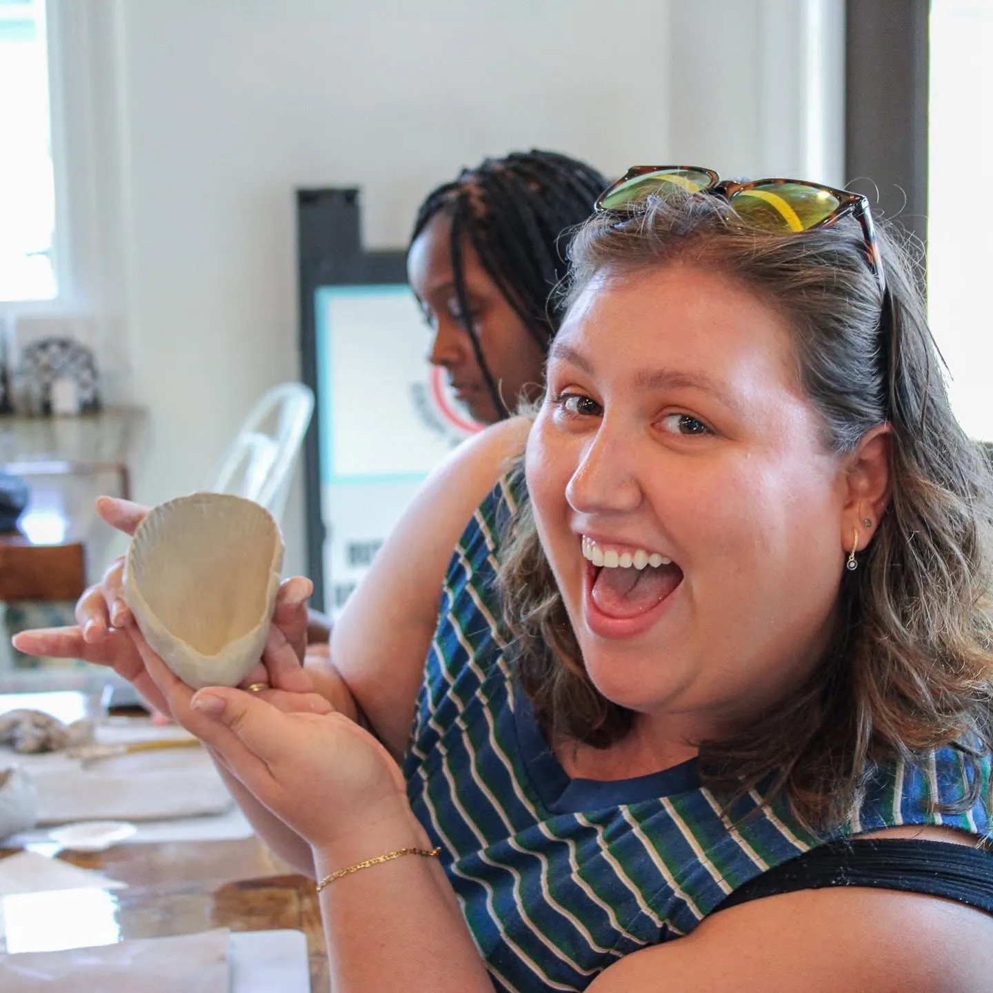 A delighted student holding the shell-shaped bowl she made at a Devine Perks class