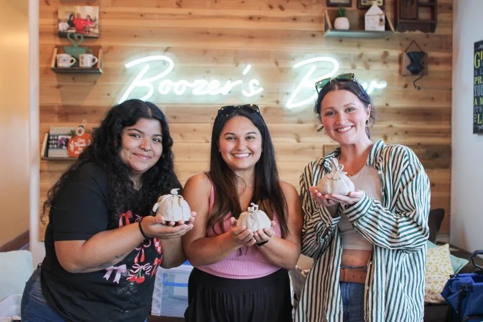 Three students smiling with the pinch-pot pumpkins they made at a Devine Perks workshop