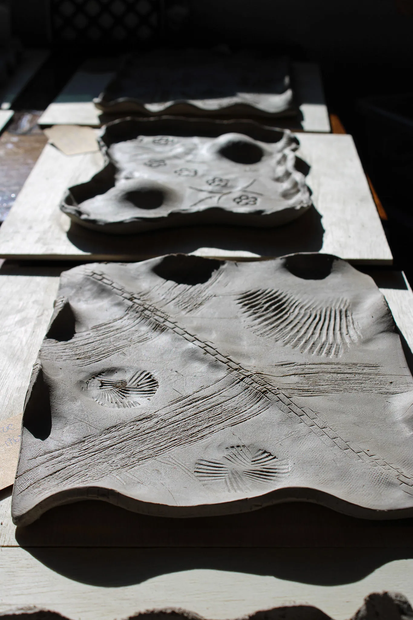 Hand-built clay trays pressed with shell and fern patterns drying in the sun